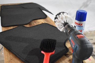 Werkzeug und Reinigungsutensilien liegen auf einer Holzoberfläche neben zwei schwarzen Matten.